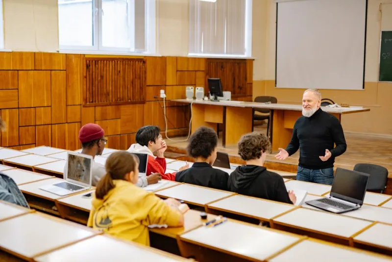Преподаватель ведёт занятие в аудитории, слушатели сидят за партами с ноутбуками